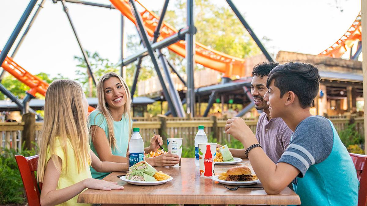 Four people sitting at a table eating under a rollercoaster at Busch Gardens in Tampa, Florida, USA